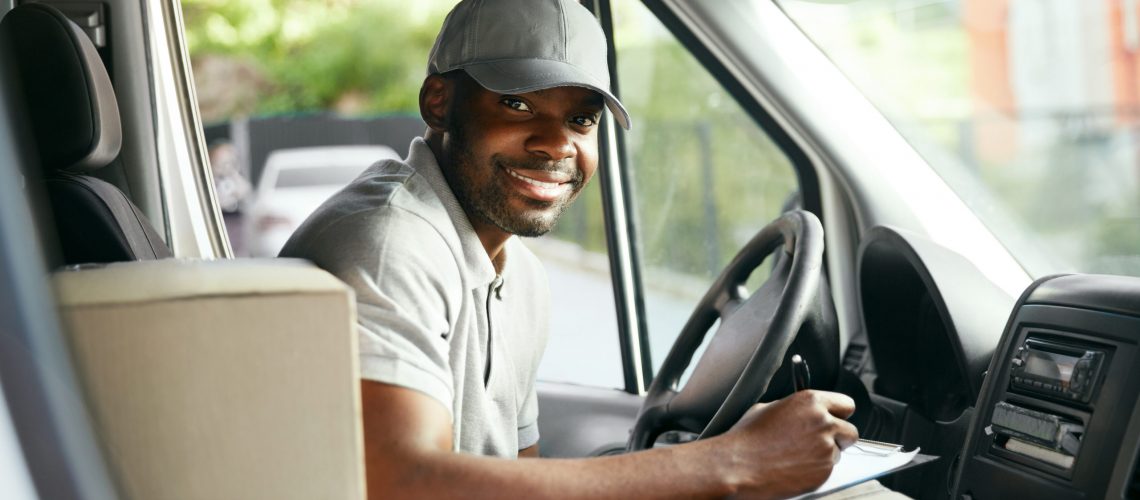 Courier Delivery. Black Man Driver Driving Delivery Car With Boxes And Packages. High Resolution